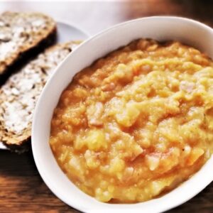 red lentil and bacon soup in bowl with buttered bread on plate