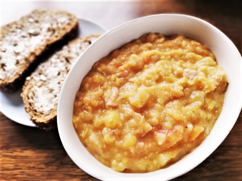 red lentil and bacon soup in bowl with buttered bread on plate