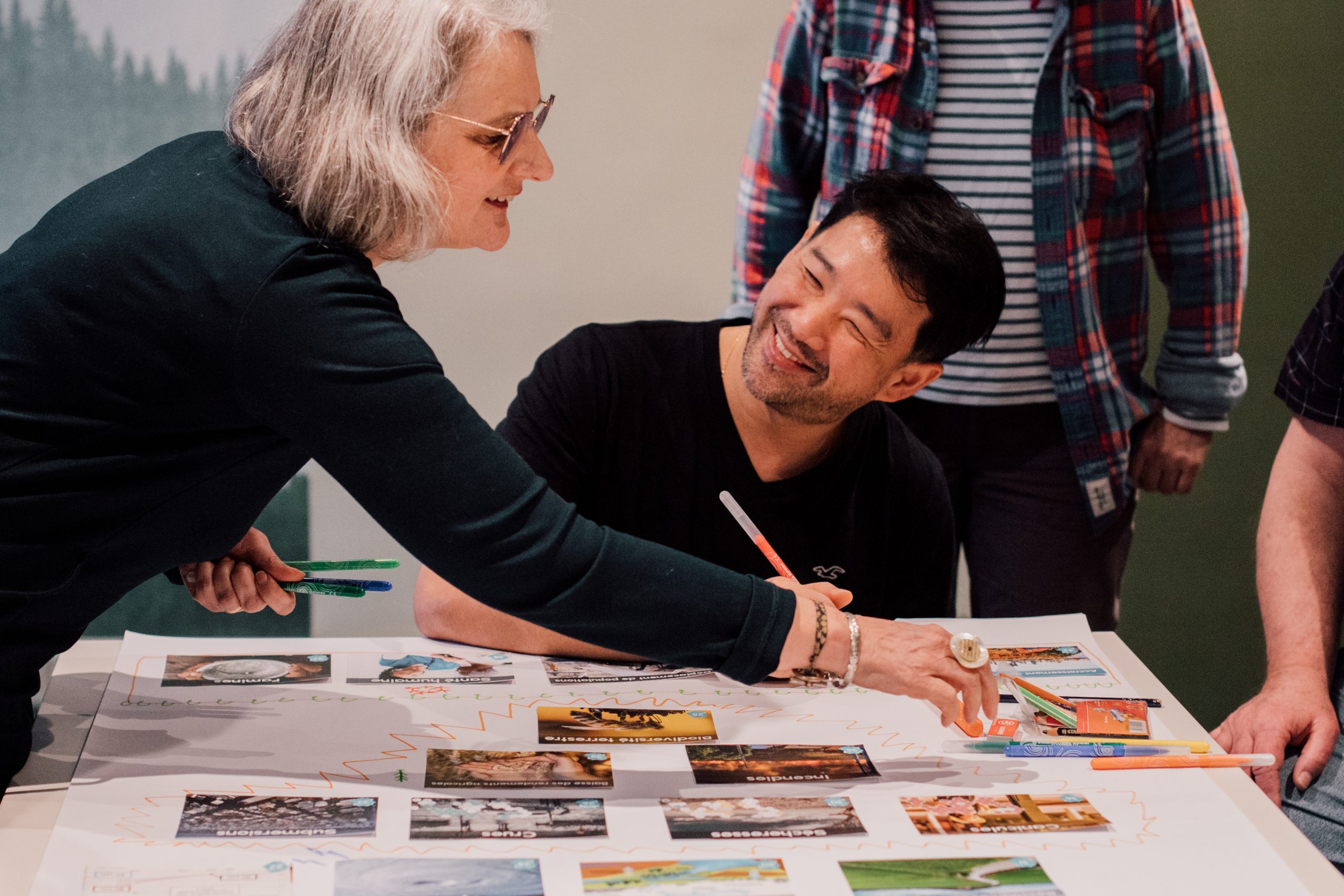 A woman and man playing the Climate Fresk card game; moving cards on a table and drawing arrows.  They look like they are having fun